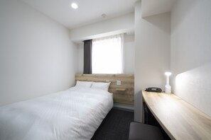 A hotel room with a single bed, a desk with a lamp, and a window with curtains.