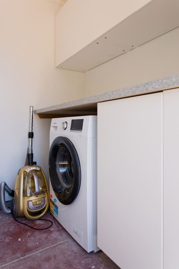 A compact laundry area with a front-loading washing machine and a vacuum cleaner.