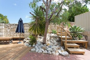 A wooden deck with a stone wall, a bench, and a staircase leading to a covered area.