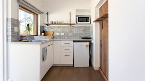 A compact kitchen with white cabinets, a built-in microwave, and a small refrigerator. - Dingo at White Gum Lodge (White Gum Valley)