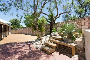 A wooden deck with stone walls and a stone wall with a wooden bench. - Emu at White Gum Lodge (White Gum Valley)