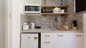 A compact kitchenette with a microwave, toaster, and coffee maker on the countertop, a sink, and a small refrigerator below.