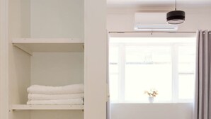 A room with a white wardrobe, a grey sofa, a window with curtains, and a hanging light fixture.