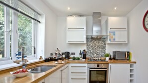 Uma cozinha moderna com armários brancos, bancada de madeira, forno Bosch e janela com vista para o verde.