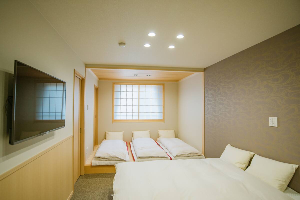 A hotel room with a large bed, a television mounted on the wall, and a window providing natural light.