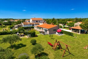 Et boligområde med huse, en terrasse med rød parasol og et legetårn.