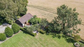 An aerial view of a house with a sloped roof, surrounded by a well-maintained lawn and dense trees.