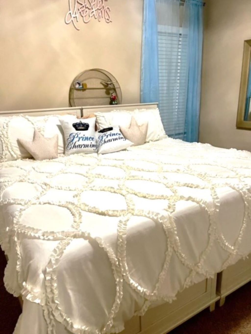 Uma cama com um edredom branco e almofadas, um espelho redondo pequeno e uma decoração na parede.