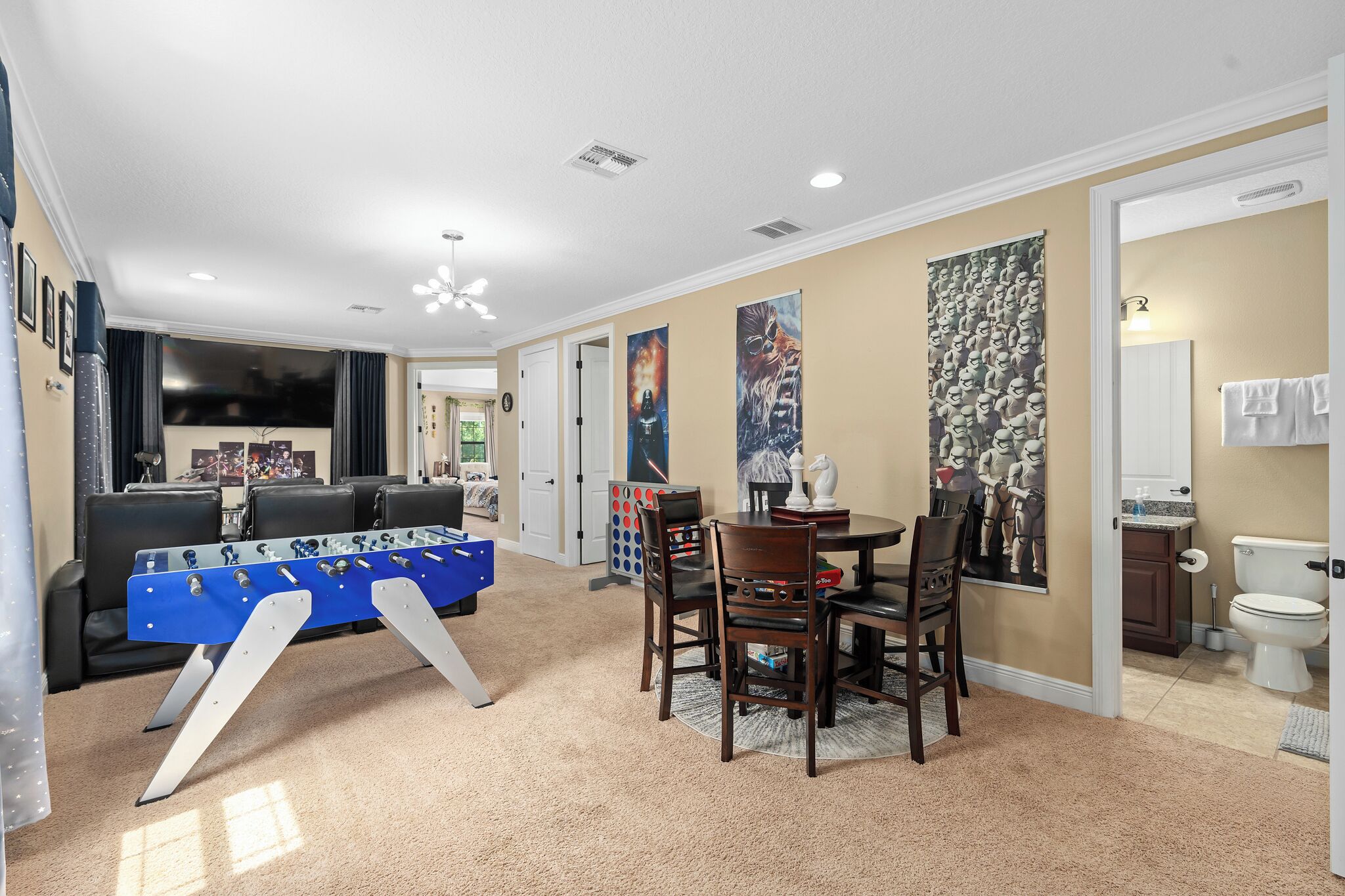 A living room with a foosball table, a dining area with chairs, and a kitchen area with a toilet visible.