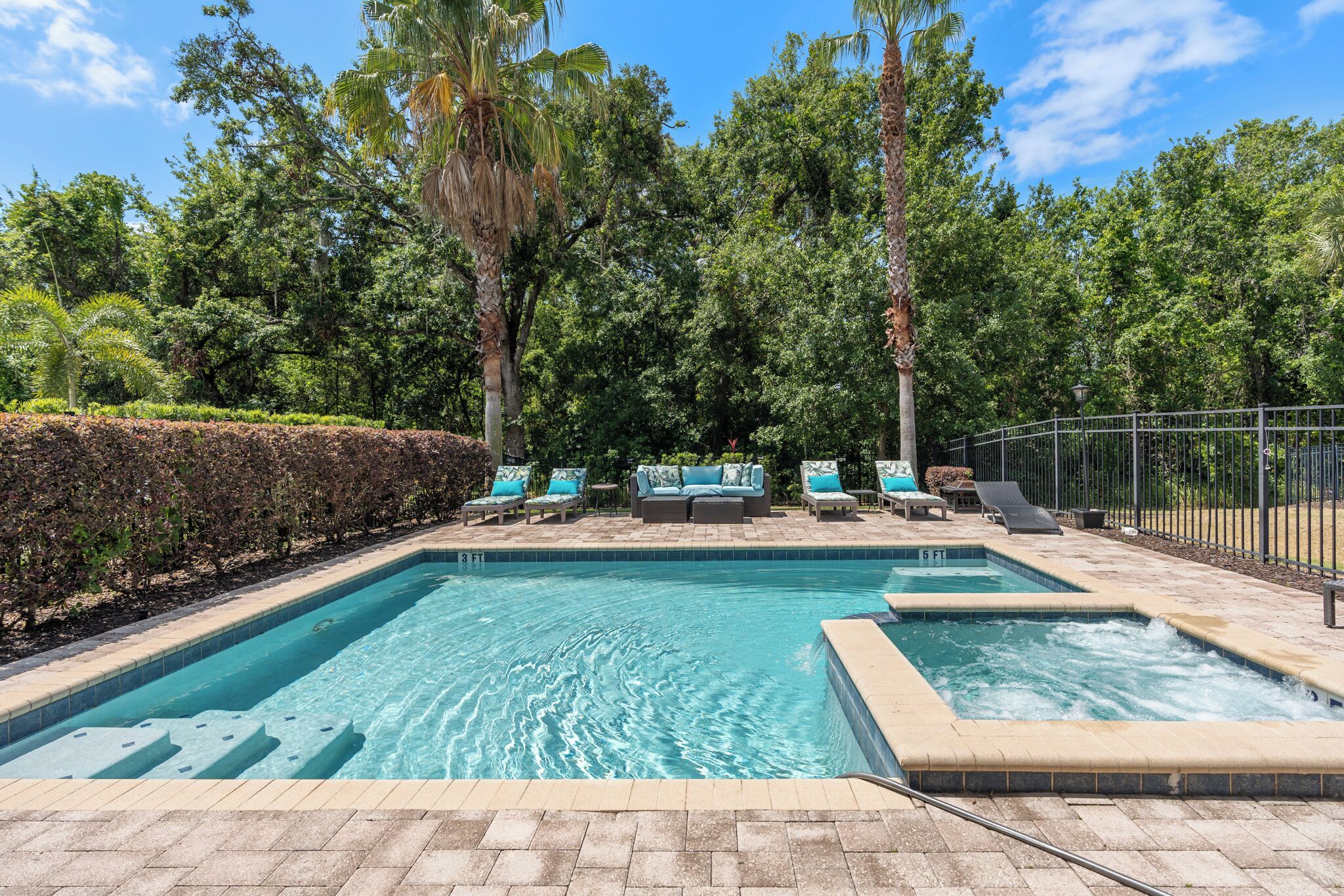 A rectangular pool with a hot tub, surrounded by lounge chairs and a sofa.