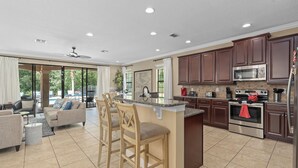 A spacious kitchen with dark wooden cabinets, a central island with bar stools, and a large island sink. - 5-bedroom ALL SUITES PET FRIENDLY Luxury home Minutes to DISNEY & THEME PARKS (Reunion)
