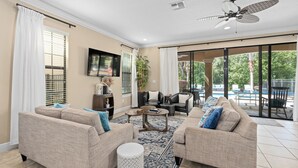 A spacious living room with beige sofas, a coffee table, and a ceiling fan. - 5-bedroom ALL SUITES PET FRIENDLY Luxury home Minutes to DISNEY & THEME PARKS (Reunion)