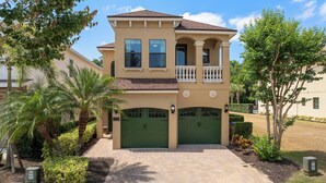 A two-story house with a balcony, green garage doors, and a paved driveway. - 5-bedroom ALL SUITES PET FRIENDLY Luxury home Minutes to DISNEY & THEME PARKS (Reunion)
