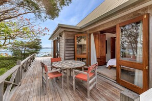 A wooden deck with a table and chairs, a bed, and a view of the sea.