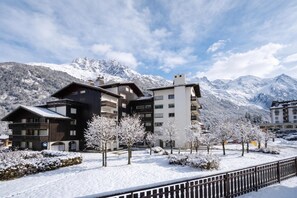 A hotel with multiple floors, snow-covered trees, and a mountain backdrop. - Apt Clos du SavoyE1 parking, WIFI, ski in/out, Chamonix, France (Chamonix)
