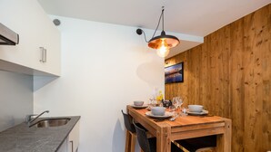 Une cuisine compacte avec une table à manger en bois pour deux personnes, un évier moderne et un luminaire suspendu.