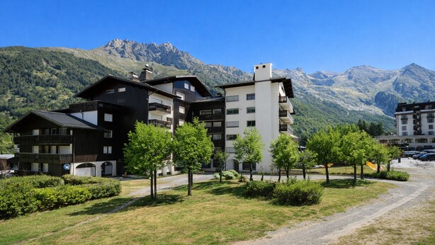 Un hôtel à plusieurs étages, doté d’un design moderne, entouré d’une végétation luxuriante et avec des montagnes en toile de fond.