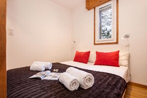 A hotel room with a bed, a window with a view of snow-covered trees, and a magazine on the bed. - Apt Clos du SavoyE1 parking, WIFI, ski in/out, Chamonix, France (Chamonix)