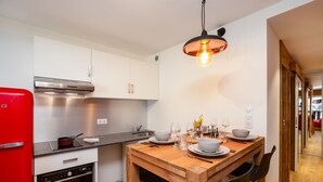 Une cuisine moderne avec des meubles blancs, un réfrigérateur rouge et une table à manger en bois, mise pour quatre personnes.