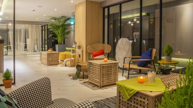 Un moderno vestíbulo de hotel con muebles de mimbre, una mesa verde con una vela y una planta grande en maceta.