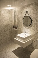 Un baño con lavamanos independiente, ducha y espejo redondo en la pared.