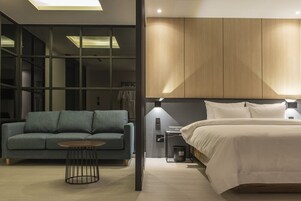 Una habitación de hotel moderna con cama, sofá, una mesita y un armario.