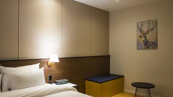 A hotel room with a bed, bedside table, lamp, artwork, and a small round table.