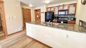 A modern kitchen with granite countertops, wooden cabinets, and a black refrigerator. - The Village At Mammoth, 2BR/2B Suite, Great Location Above Shops & Restaurants   (Mammoth Lakes)