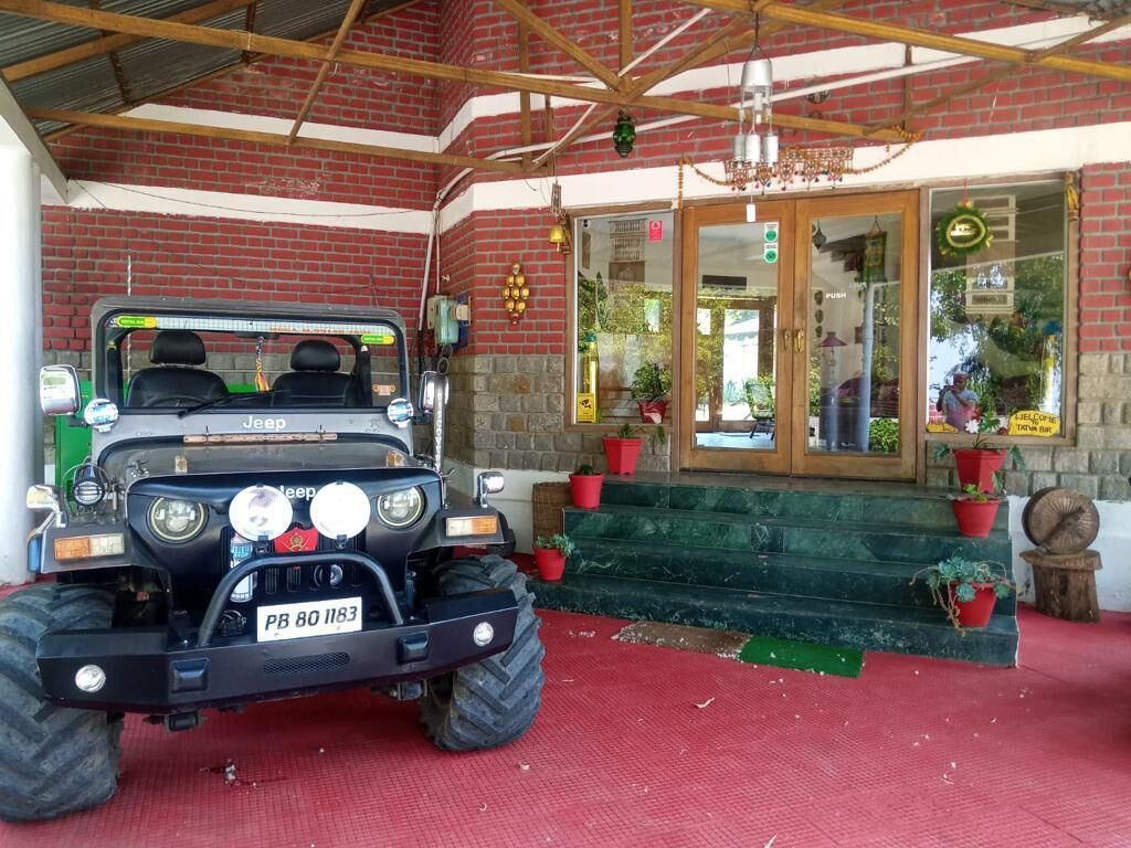 Un Jeep estacionado frente a un edificio de fachada de ladrillo, una escalera de madera y macetas con plantas.