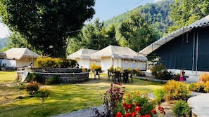A courtyard with tents, a stone wall, and a small garden with flowers. - Tatva Bir Tents and Hotel (Baijnath)