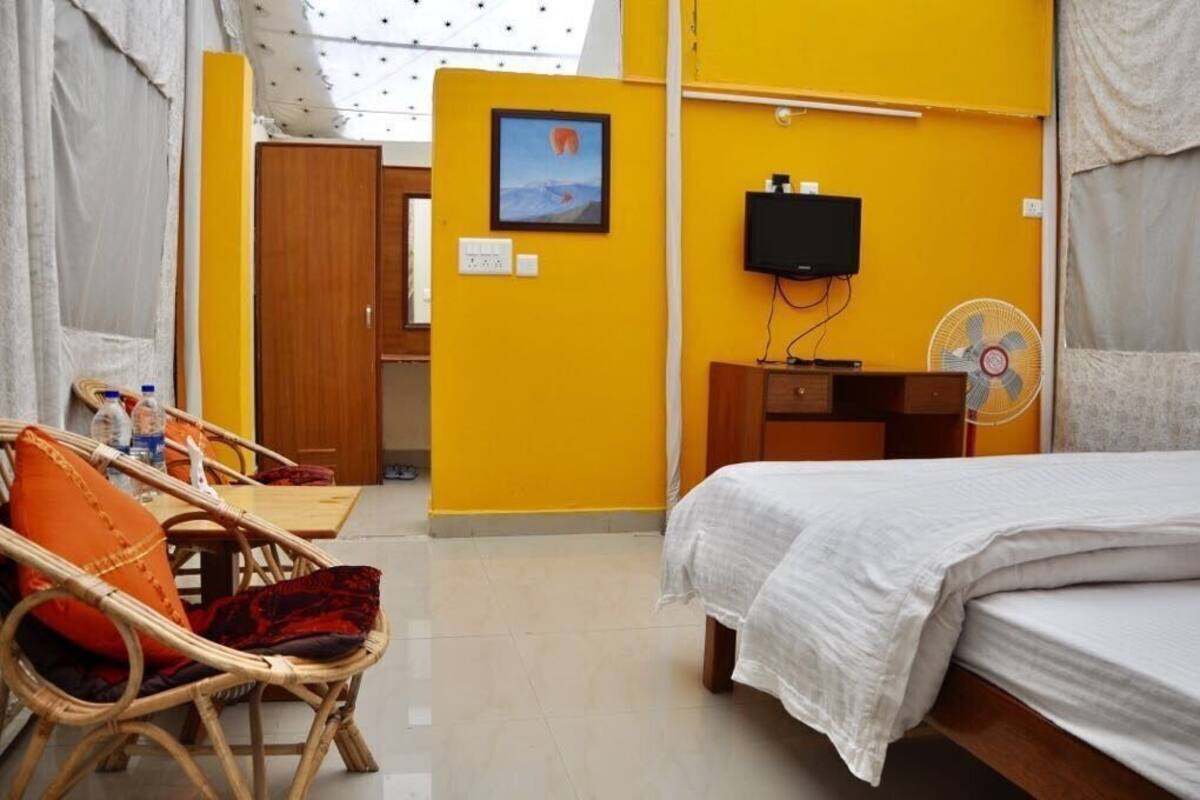Une chambre comprenant un lit, une télévision, un ventilateur et un coin repas avec des chaises et une table.