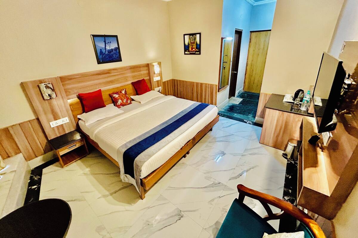 Une chambre d’hôtel comprenant un lit, des tables de chevet, un bureau avec une chaise, un miroir et une porte donnant sur un couloir.