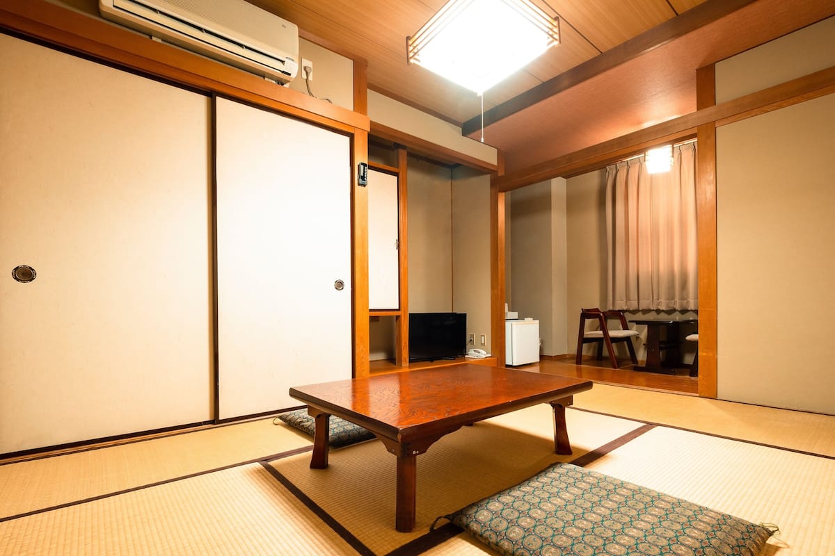 Um quarto japonês tradicional com tatames, uma mesa de madeira baixa, uma televisão e um frigorífico.
