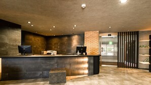 A reception area with a counter, two monitors, a brick accent wall, and a glass door leading outside. - Business Hotel Hane Ise Inter (Ise)