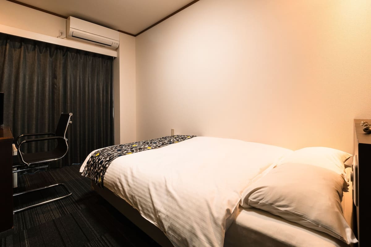 Quarto de hotel com cama, cadeira, escrivaninha e ar condicionado.