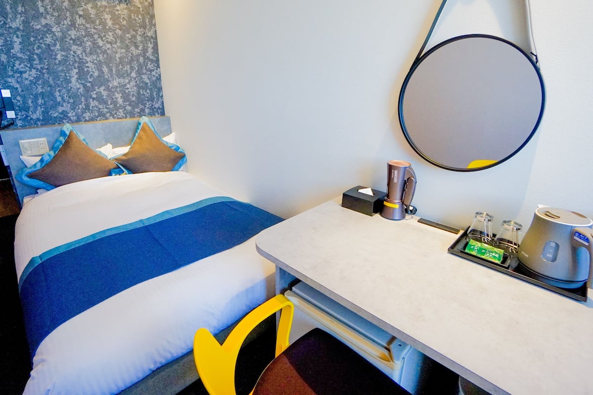 Quarto de hotel com cama, mesa de cabeceira e escrivaninha, incluindo cafeteira e chaleira.