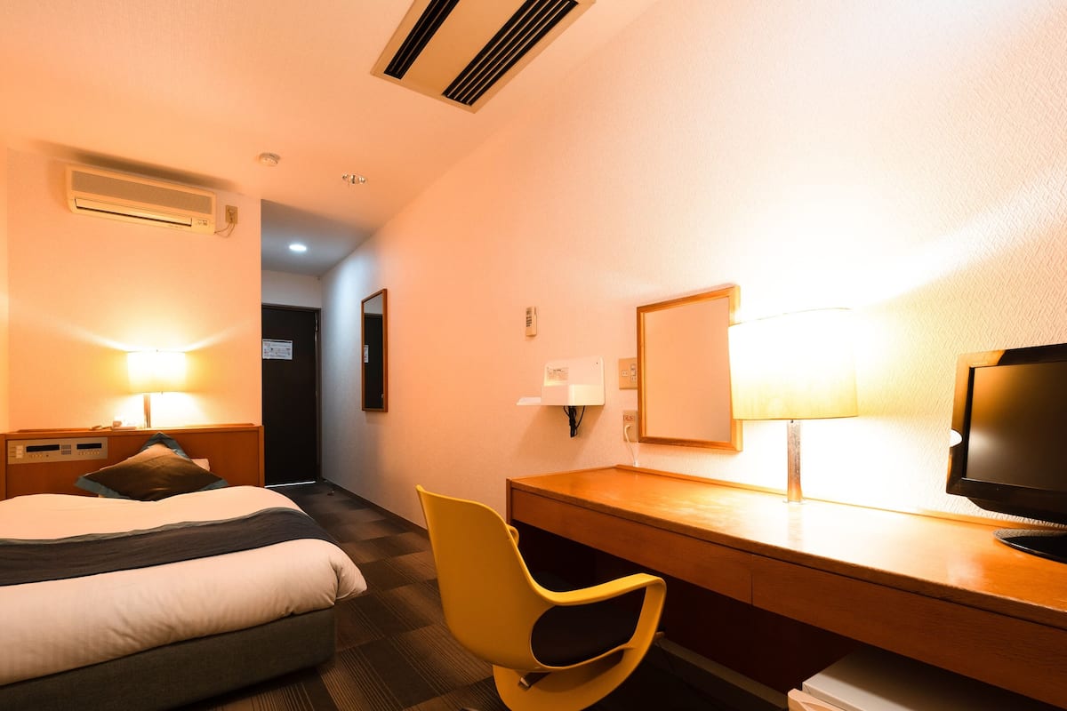 Quarto de hotel com cama, escrivaninha, cadeira, televisão e frigorífico.