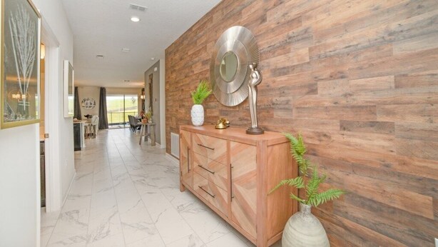A hallway with a wooden wall, a marble floor, a wooden cabinet with drawers, a mirror, and a potted plant.