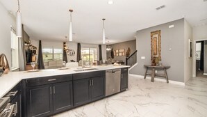 A spacious kitchen with a large island, dark cabinetry, and a marble floor.