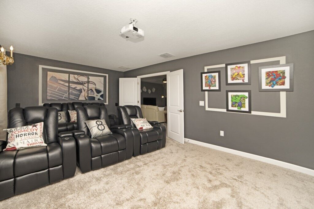 A home theater room with a black leather recliner sofa, a ceiling projector, and framed artwork on the walls.