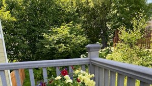 A white wicker chair on a wooden deck with a railing, surrounded by greenery and a wooden fence. - Gracie's Homer House; Home With A View (Homer)