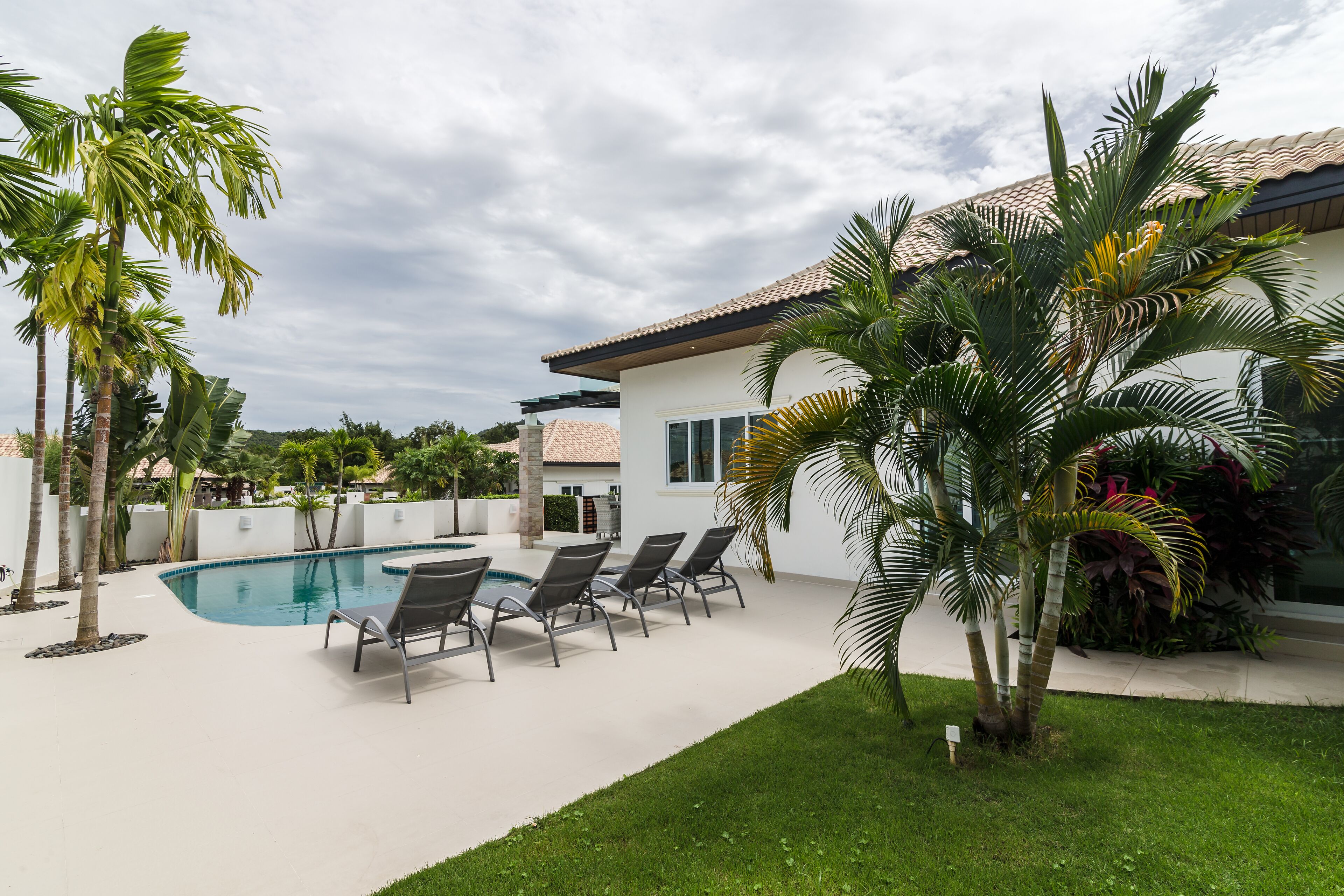 A swimming pool with lounge chairs, palm trees, and a house with a tiled roof.