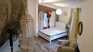 Une chambre à coucher avec un lit, un ventilateur, une chaise, une horloge murale et une fenêtre avec des rideaux.