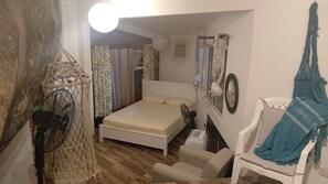 Une chambre à coucher comprenant un lit, une chaise, un luminaire suspendu, une horloge murale et une fenêtre avec des rideaux.