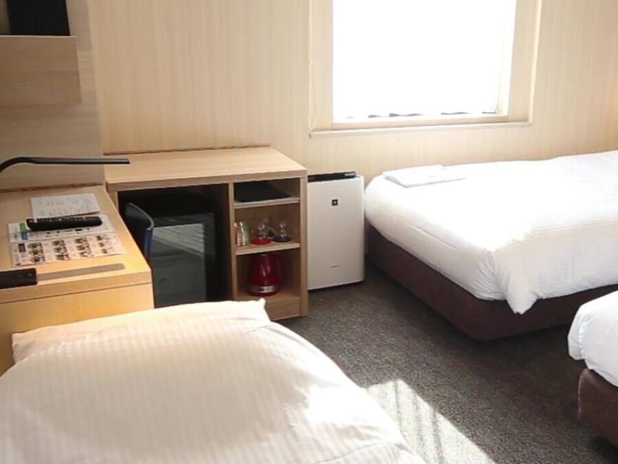 A hotel room with two beds, a desk with a computer, a coffee machine, and a window.