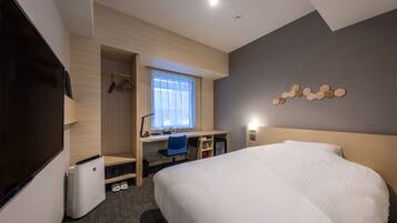 A modern hotel room with a large bed, a desk with a chair, a wardrobe, and a window with curtains.