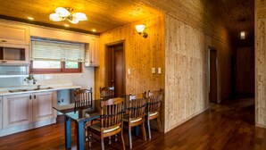 A wooden interior with a dining table and chairs, a kitchen area with cabinets and a window, and a wooden floor. - Witch's  broomstick Pension (Jeju City)