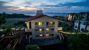 A two-story building with a stone facade, multiple balconies, and a view of the sea at dusk. - Witch's  broomstick Pension (Jeju City)