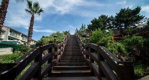A wooden staircase leading uphill, surrounded by greenery and a clear sky. - Witch's  broomstick Pension (Jeju City)