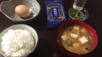 Una mesa con un tazón de arroz blanco, un tazón de sopa de tofu, un paquete de algas marinas y un vaso de agua, junto con un huevo crudo.